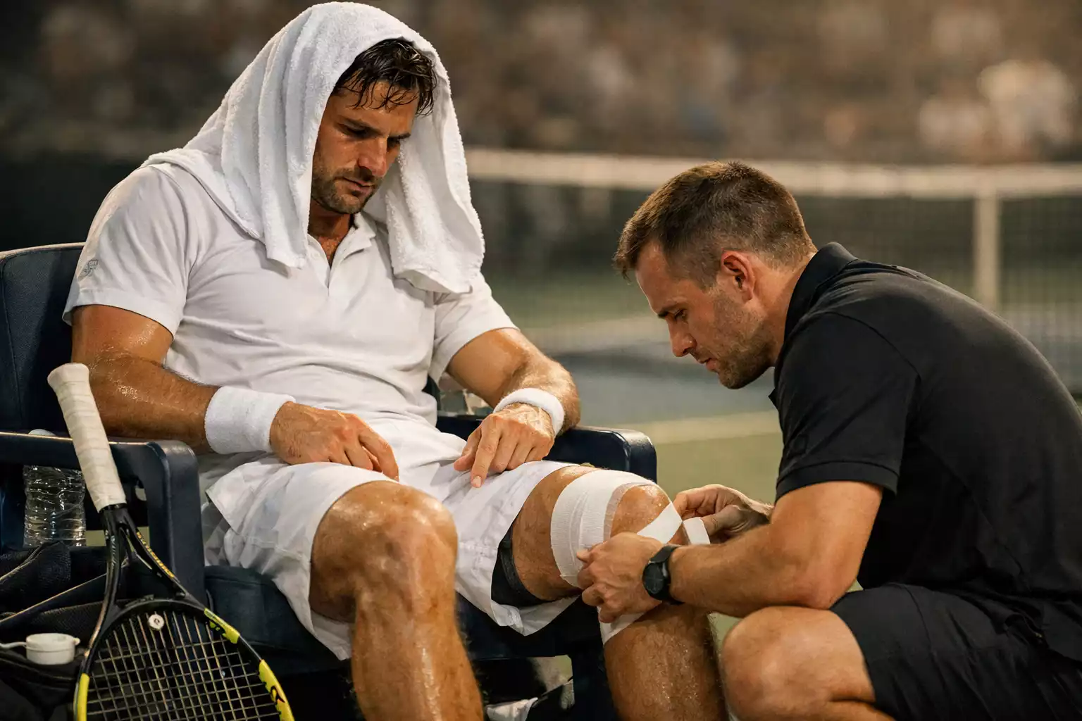 Jugador de tenis sentado en la silla de descanso con una toalla sobre la cabeza y tratamiento médico en la rodilla durante un partido
